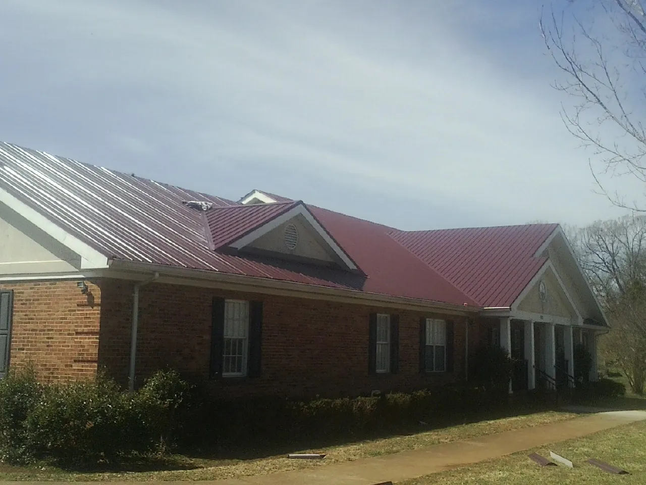 Red metal roof with gabled entries on a long brick building, from a Hail Damage Roof Repair job in Fishertown