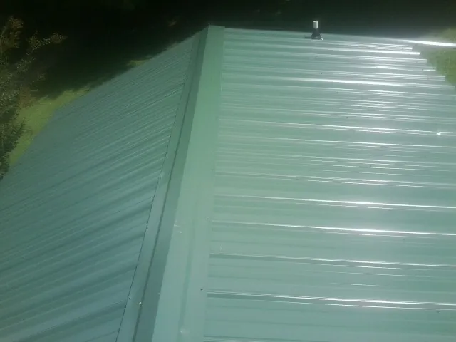 New green metal panels meeting at the ridge of a roof — Flat Roof Repair work by our crew in Fishertown