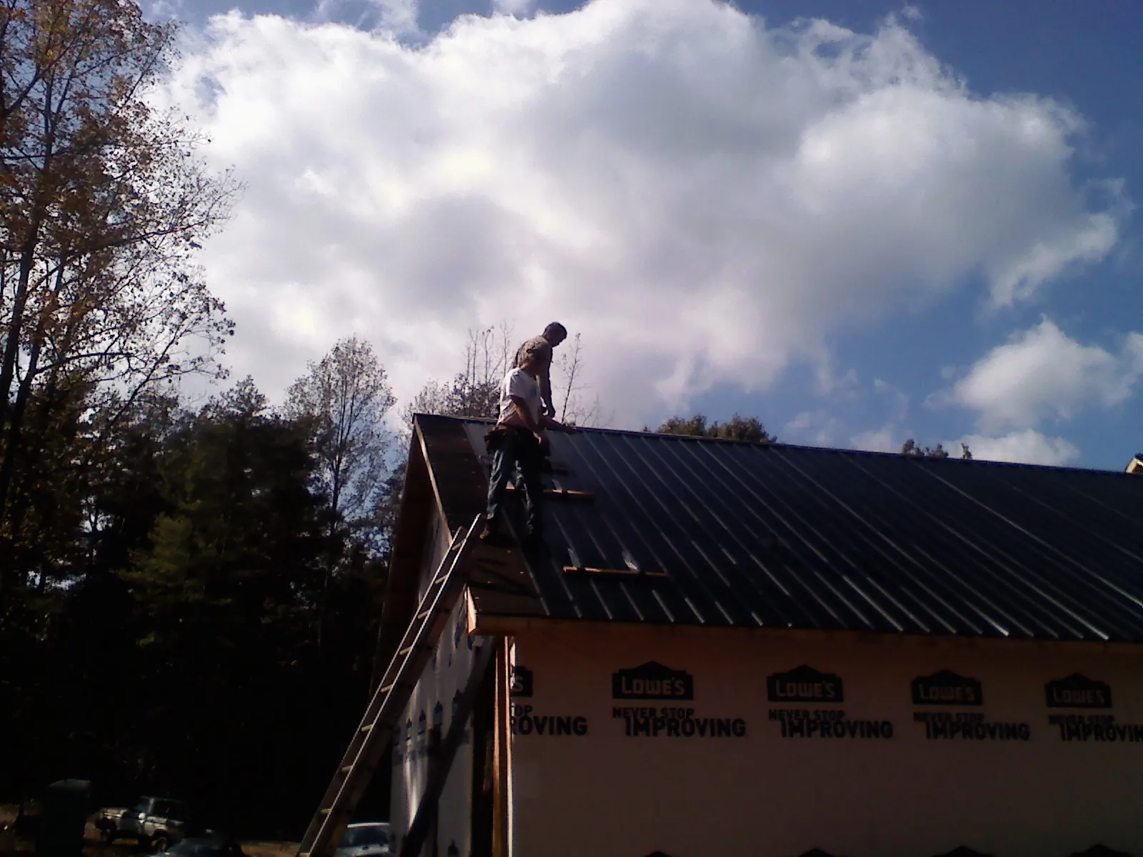 Roofer fastening dark metal panels high against a cloudy sky, from a Roof Inspection job in Fishertown