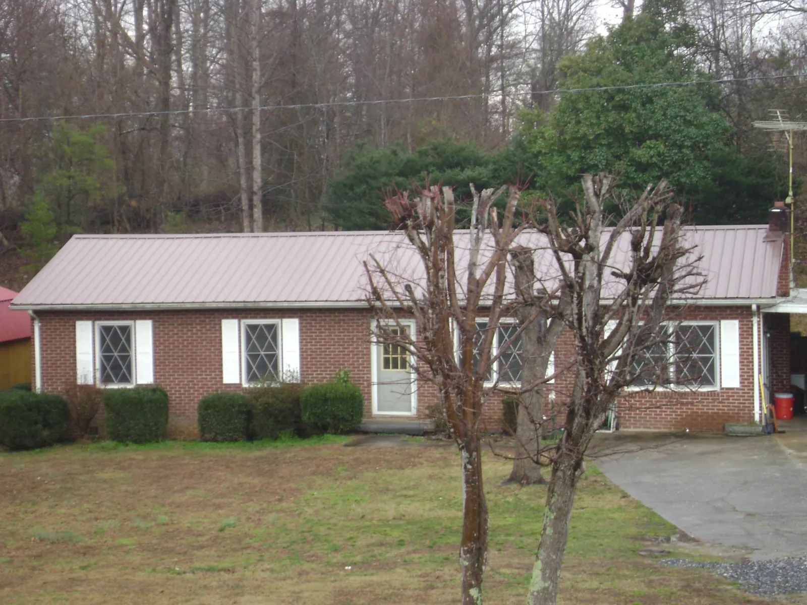 Mauve metal roof on a brick ranch home behind bare trees in Fishertown
