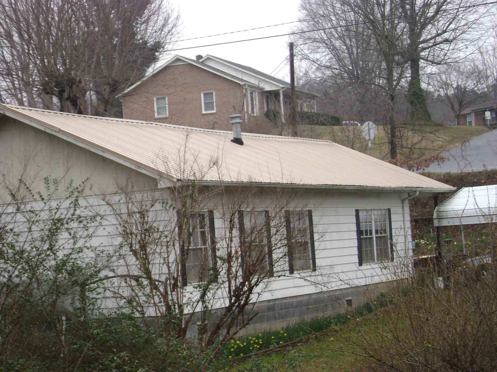 Tan metal roof on a white sided house set into a hillside — Commercial Roofing by Roofing Brothers in Fishertown